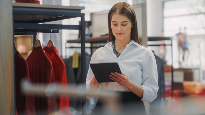 A clothing shop assistant checking a tablet beside the rails during the shift